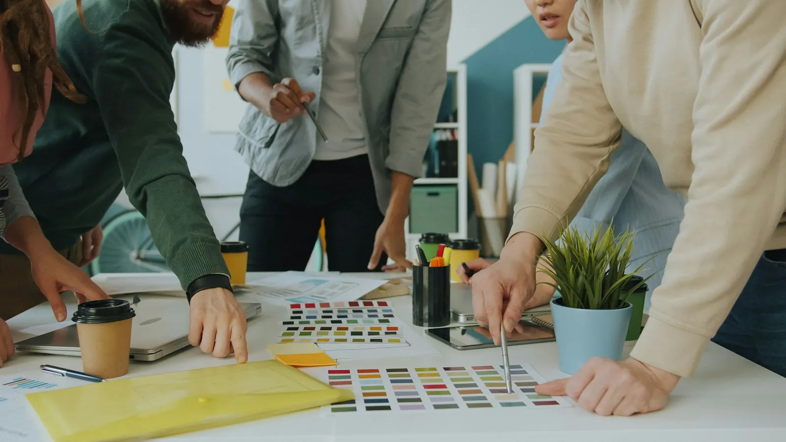 A design team gathered around a table, pointing at colour swatches and printed page layouts